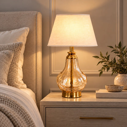 Amber glass table lamp illuminated beside a bed
