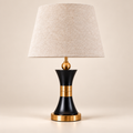 Black and gold hourglass table lamp with a light linen shade