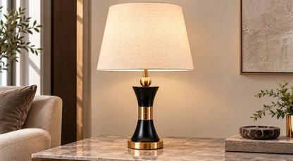 Black and gold hourglass table lamp on a marble console beside a sofa