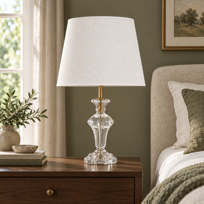 Faceted crystal pedestal table lamp on a walnut bedside table beside a neutral upholstered bed