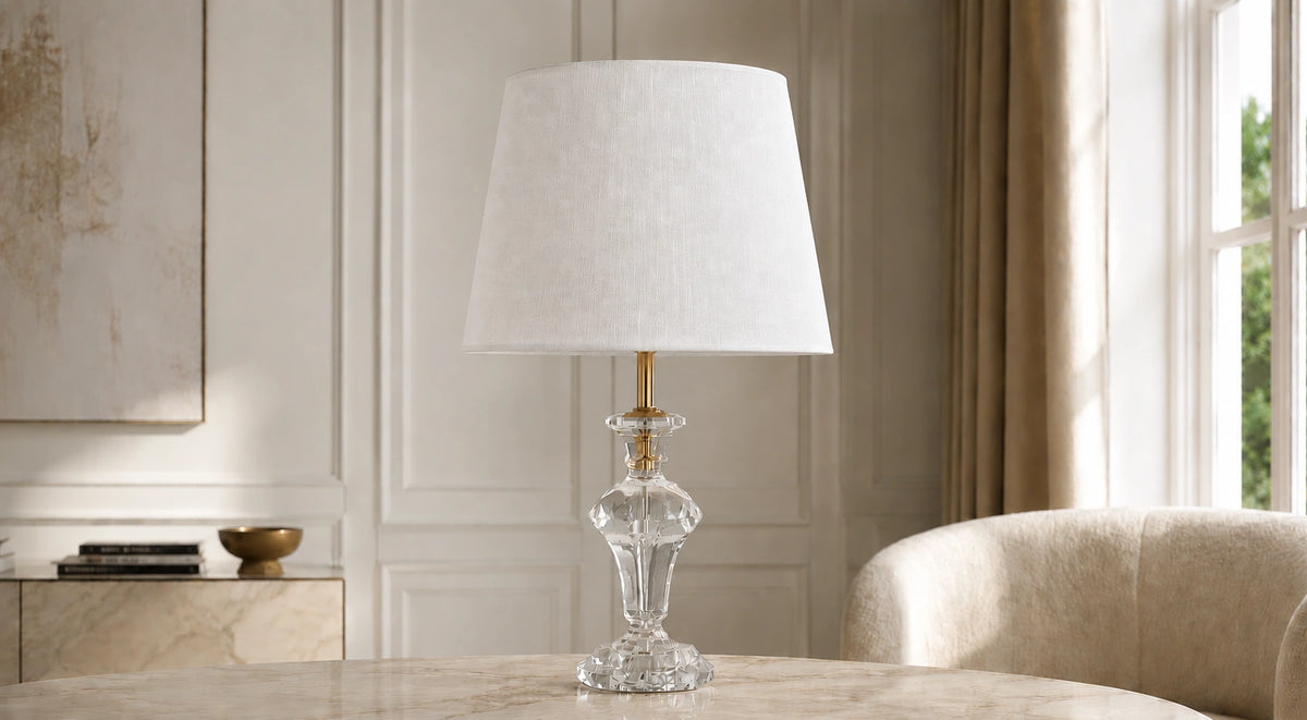 Crystal pedestal table lamp on a pale console beside a cream chair