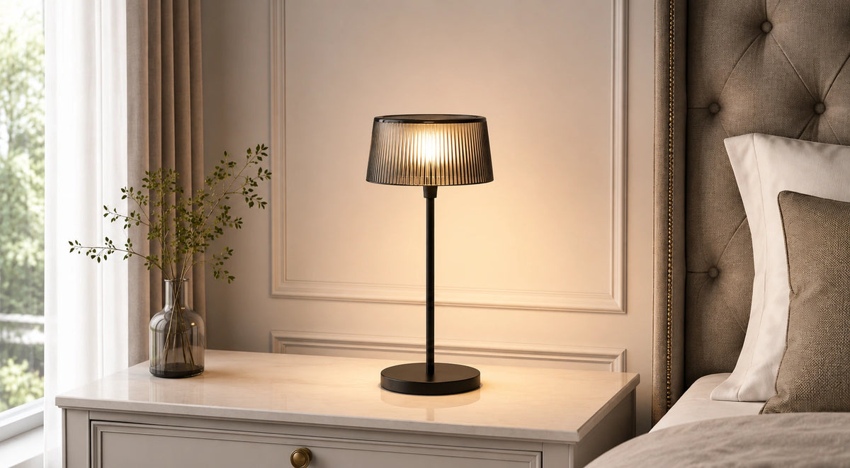 Noir Ribbed black table lamp illuminated on a bedside table