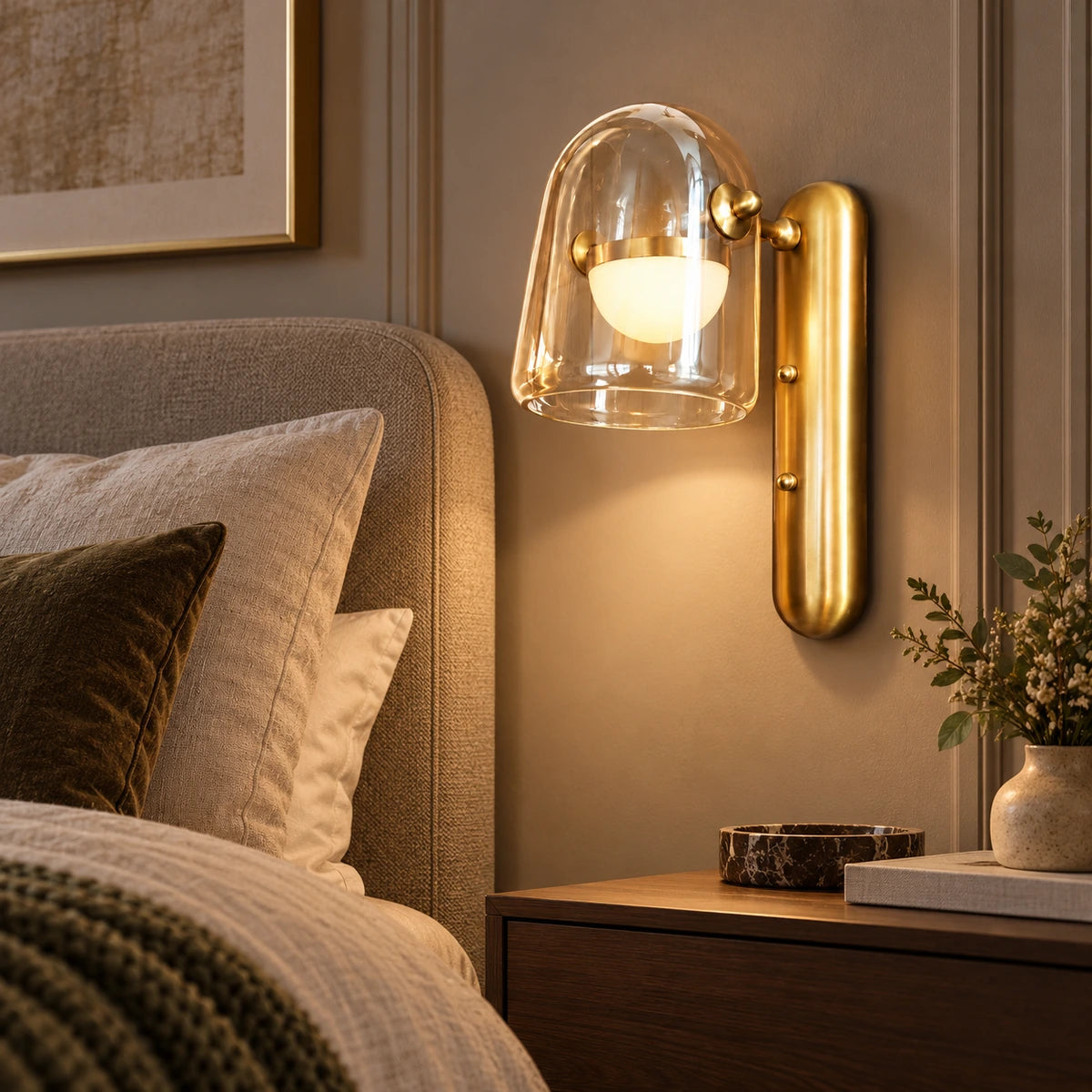 Clear glass and brushed-gold wall light beside a bed