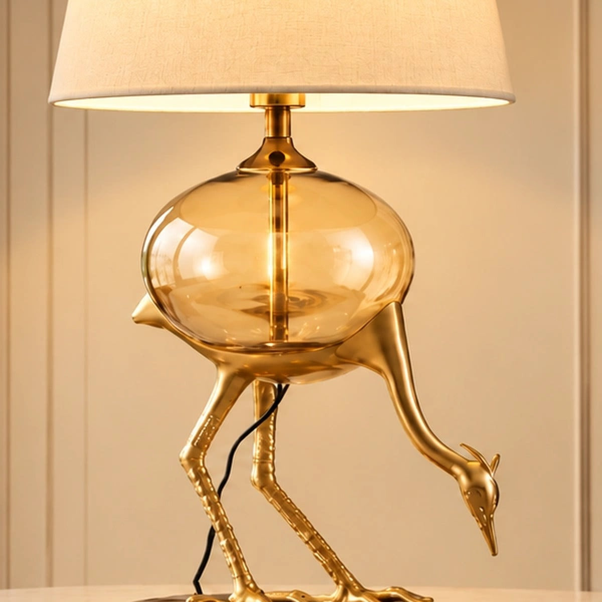 Close-up of the Aurelia crane lamp's amber glass globe and gold-tone sculpted bird detail