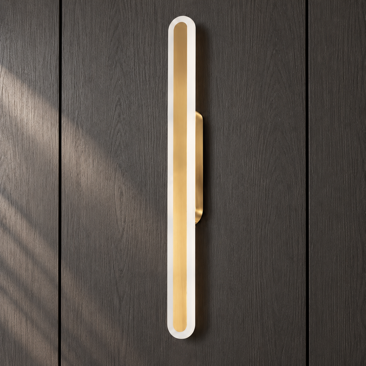 Close-up of the Luma Loop wall light's white acrylic loop, brushed-gold centre strip and compact bracket