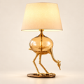 Aurelia gold-tone crane table lamp with amber glass body on a clean warm-white background