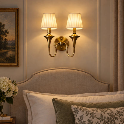 Double arm tapered shade wall sconce beside an upholstered bed