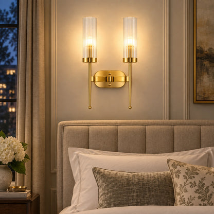 Twin ribbed glass cylinder wall sconce beside an upholstered bed