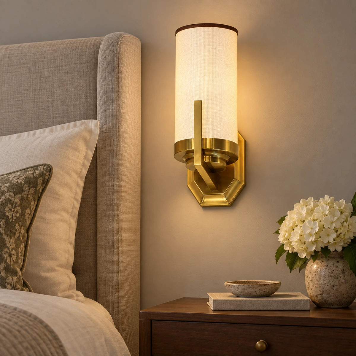 Cylinder shade wall sconce beside an upholstered bed