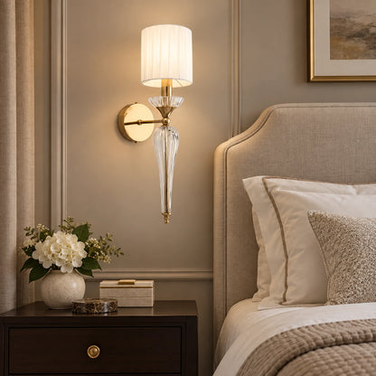 Faceted clear-stem shade wall sconce beside a bed