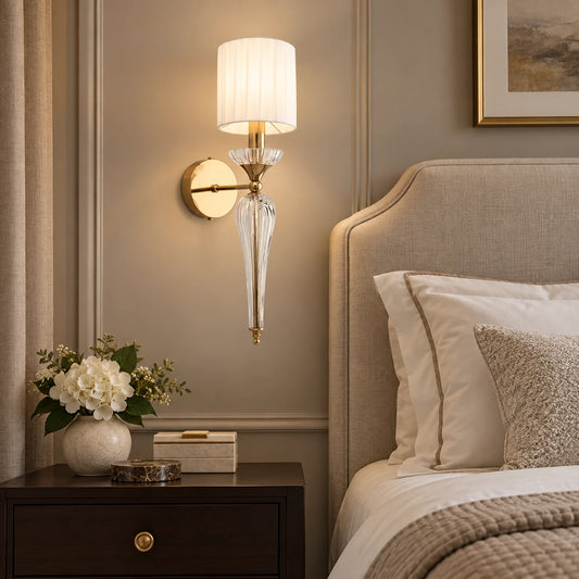 Faceted clear-stem shade wall sconce beside a bed