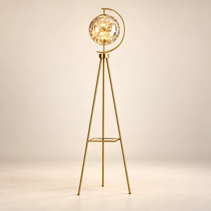 Gold-tone tripod floor lamp with a patterned glass globe and flat shelf