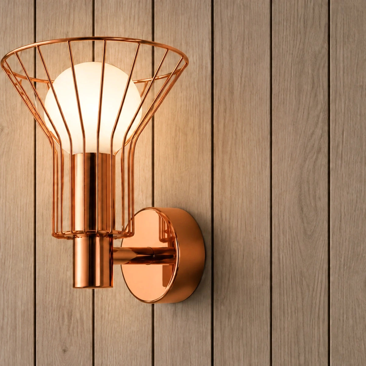 Rose-gold wire-cage globe wall light illuminated