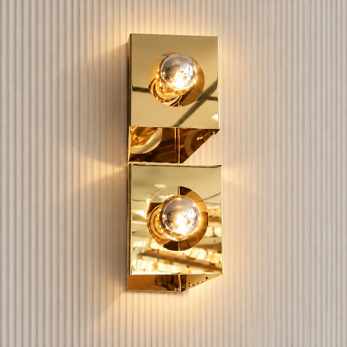 Twin-globe polished gold wall light illuminated on a fluted wall