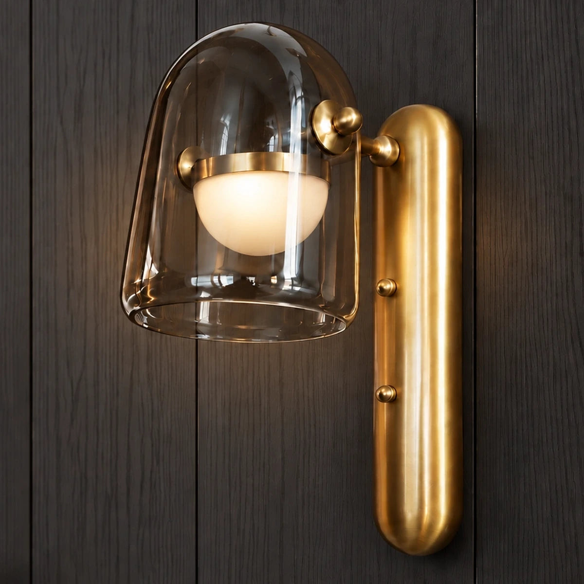 Smoked glass and brushed-gold capsule wall light illuminated