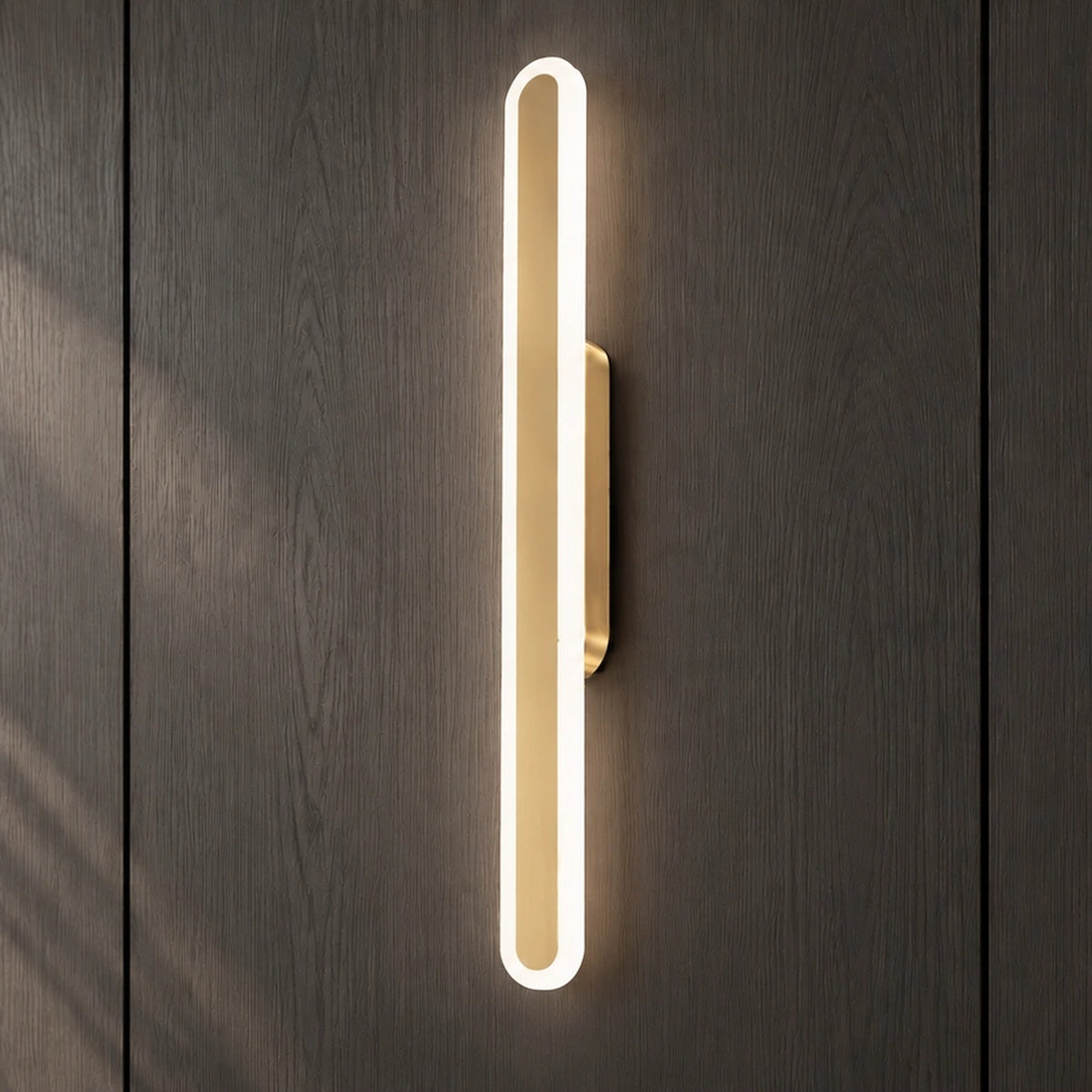 Square product view of the Luma Loop vertical LED wall light illuminated on a dark wood wall